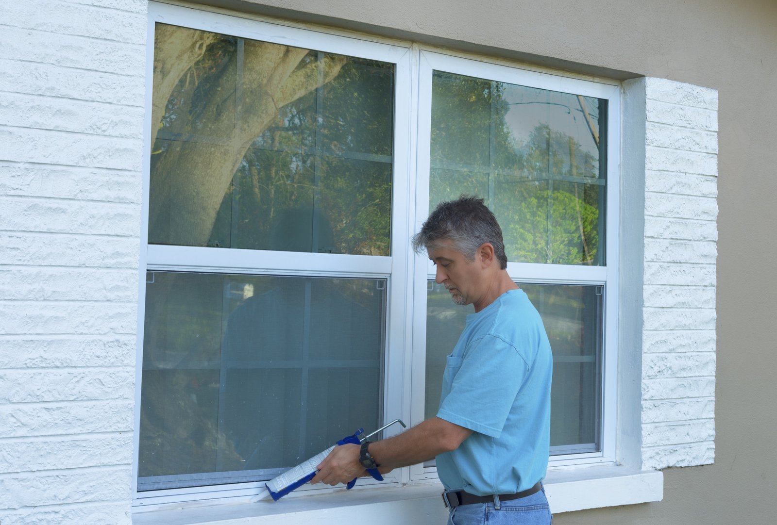 Homeowner caulking window with a caulk gun, an important part of weatherproofing homes and houses against rain, wind, hurricanes and storms.